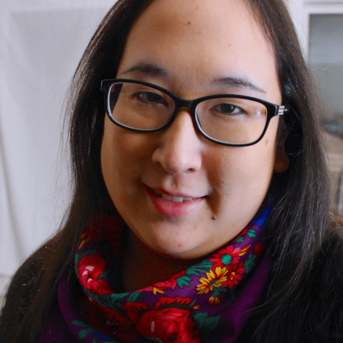 Person wearing glasses and a colourful scarf, smiling softly indoors.