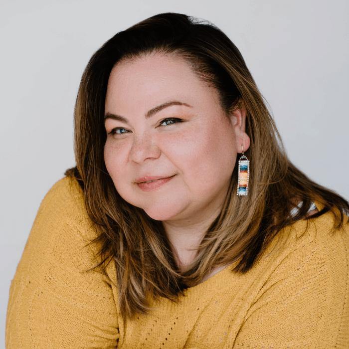 Jessie Anthony with shoulder-length brown hair wearing dangly earrings and a dark yellow shirt.