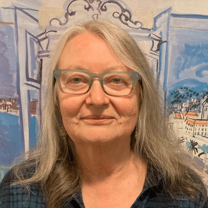 Maureen Levitt with long white and brown hair wearing glasses and a blue flannel shirt.