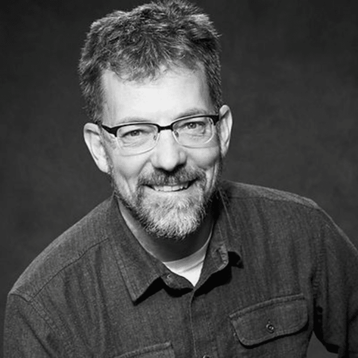 Black and white of Michael Brown with short dark hair, beard and moustache, wearing a dark button-up shirt with a white shirt underneath.
