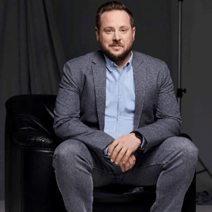 Scott Lepp seated with short brown hair, wearing a grey suit and blue shirt.