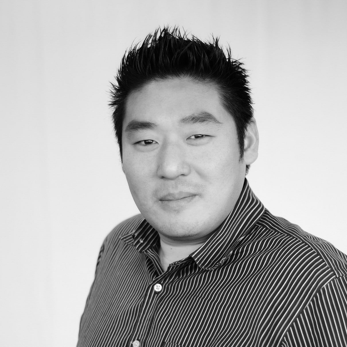 Black and white photo of Arnold Lim. He has short spiky dark hair and is wearing a striped, button-up collared shirt.