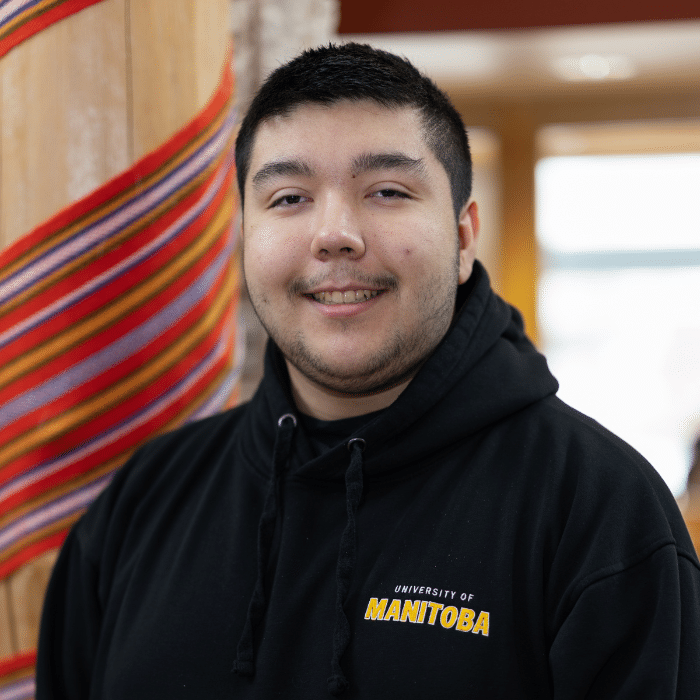 Cyrus Maytwayashing smiling indoors wearing a black University of Manitoba hoodie