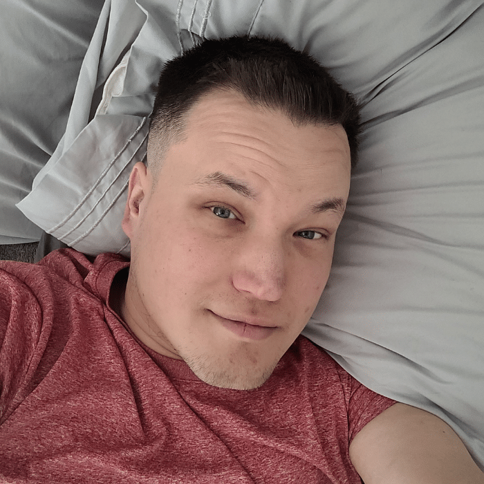 Person lying on a pillow, wearing a red shirt, looking at the camera.