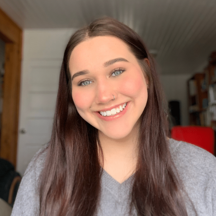 Person with long brown hair smiling at the camera indoors.