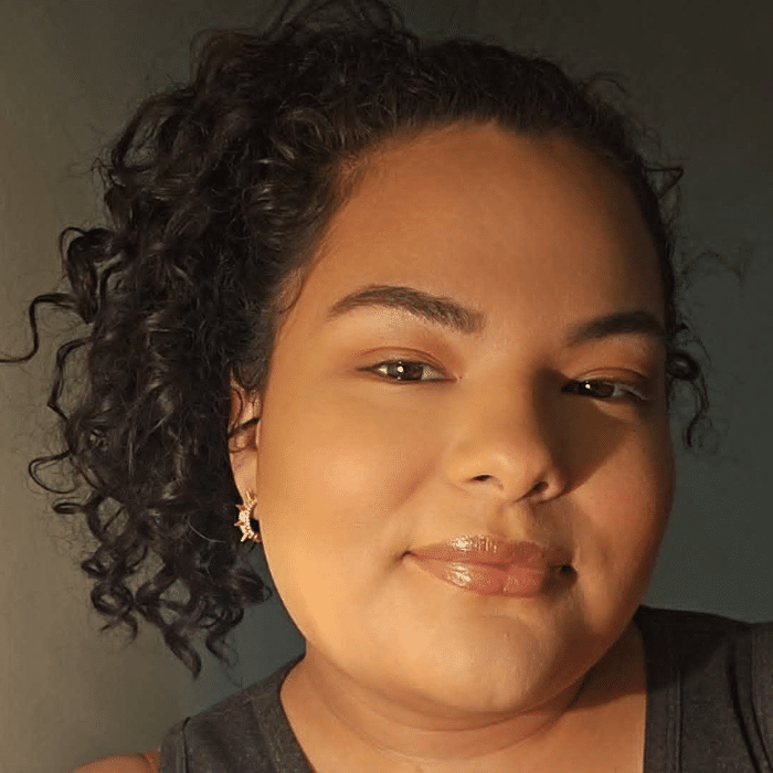 Person with curly hair and earrings in warm lighting, looking at the camera.