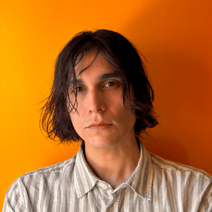 Person with medium-length dark hair standing in front of an orange wall.