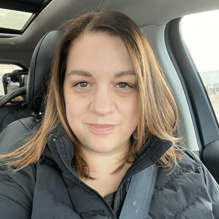 Person sitting in a car wearing a black jacket, looking at the camera.