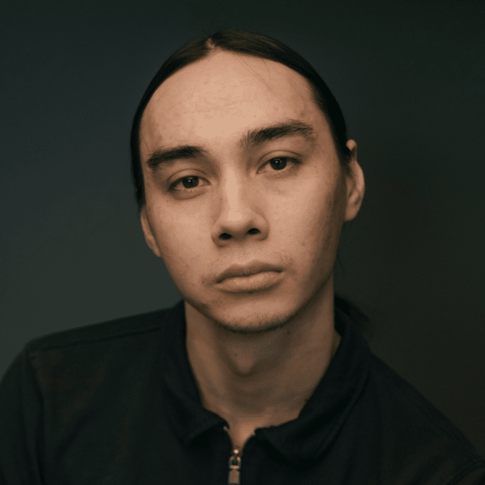 Cole Clark posing in a studio portrait wearing a black jacket against a dark background