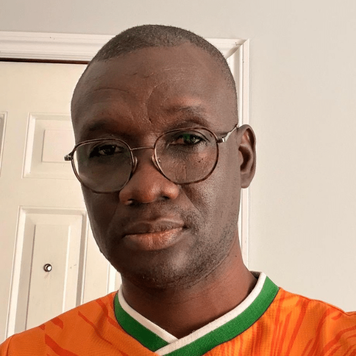 Noel Coulibaly wearing glasses and an orange jersey in an indoor portrait