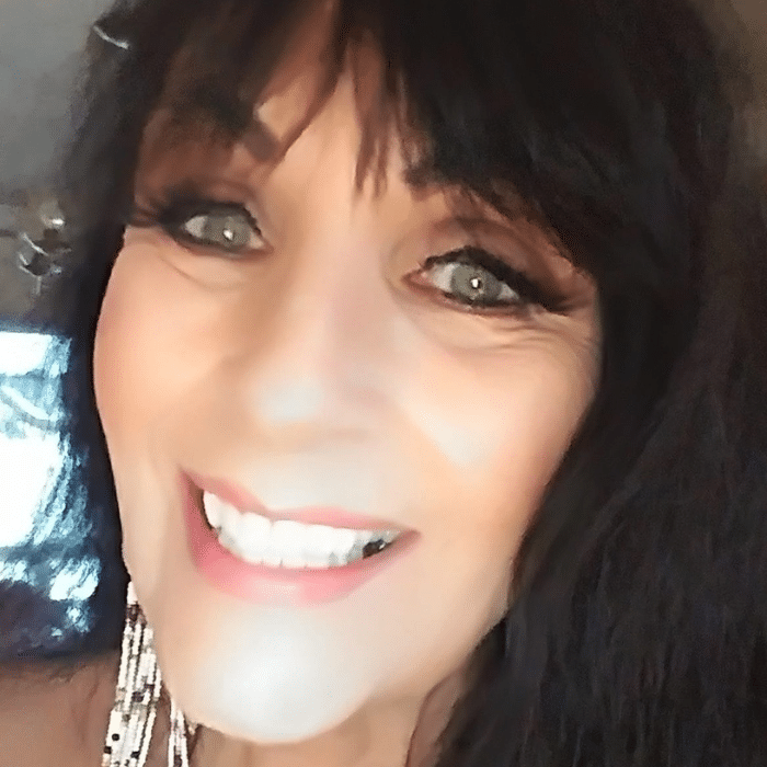 Kim Coltman smiling in a close-up portrait with dark hair and beaded earrings