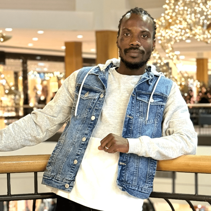 Harold Kouton leaning on a railing in a shopping centre wearing a denim vest over a grey hoodie