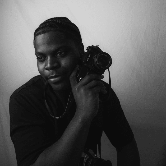 Loic Matabishi holding a camera in a black-and-white portrait