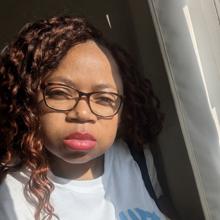 Prudence Mouafo wearing glasses and a white shirt in sunlight near a window
