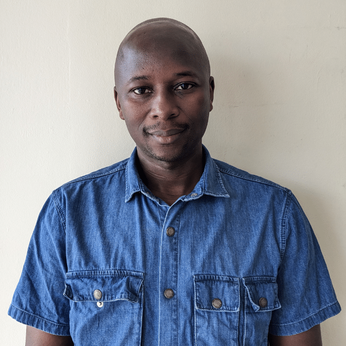 Bédier Pangnyere smiling in a portrait wearing a blue button-up shirt against a light background
