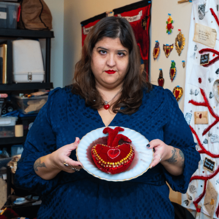 Daniela Smith-Fernandez holding a decorative heart-shaped artwork on a plate in a studio space