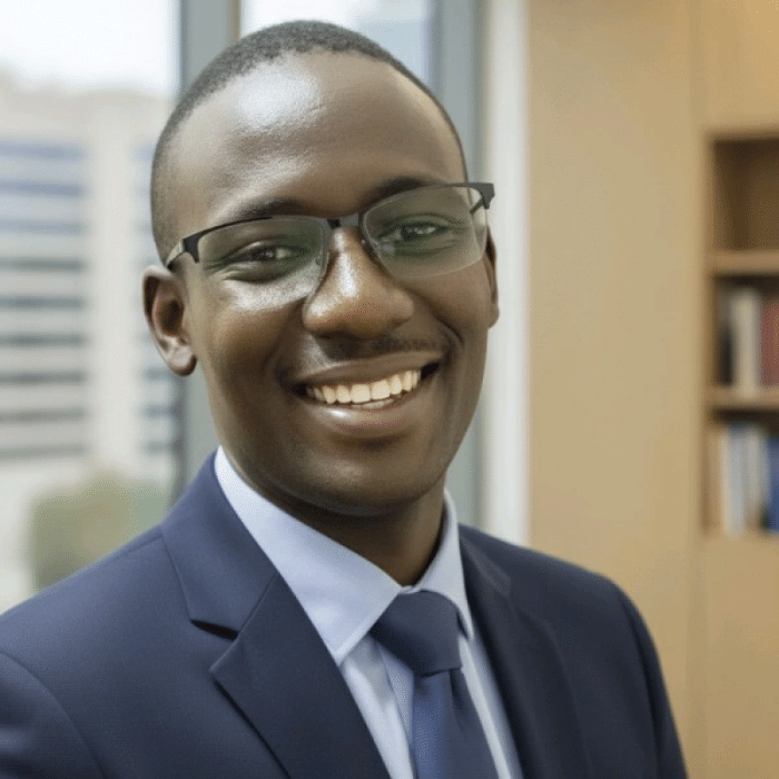 Ousmane Sambou smiling in a suit and tie in an office setting