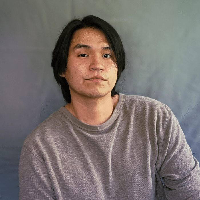 Tyrell Rowan posing in front of a grey backdrop wearing a light grey shirt